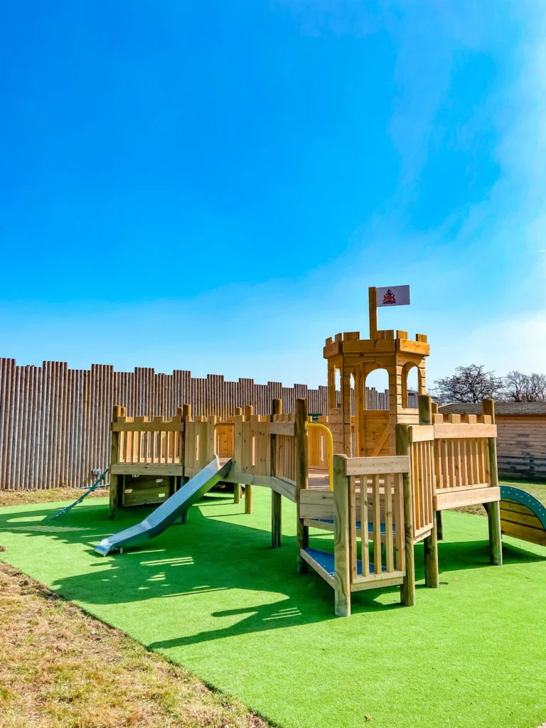 Knebworth Adventure Playground for younger children with slides and climbing platforms on bright green turf under a clear blue sky.